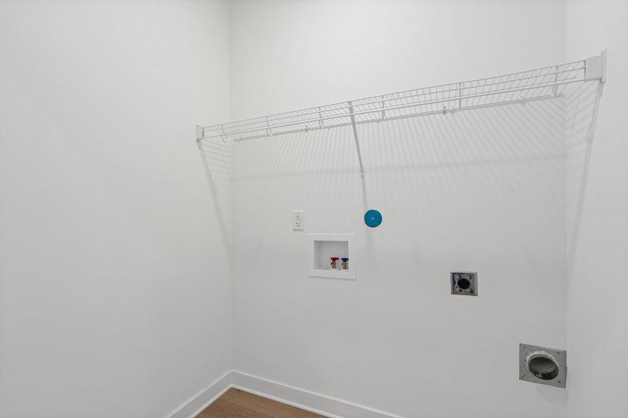Dedicated laundry area featuring a white wire shelf, washer and dryer hookups, and wood-finish flooring Dedicated laundry area featuring a white wire shelf, washer and dryer hookups, and wood-finish flooring