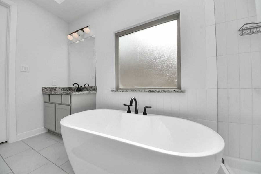 This bathroom features a modern freestanding tub, a granite-topped vanity with sleek fixtures, and a large frosted window for natural light. The clean white tiles and minimalistic design create an elegant, spa-like atmosphere. This bathroom features a modern freestanding tub, a granite-topped vanity with sleek fixtures, and a large frosted window for natural light. The clean white tiles and minimalistic design create an elegant, spa-like atmosphere.