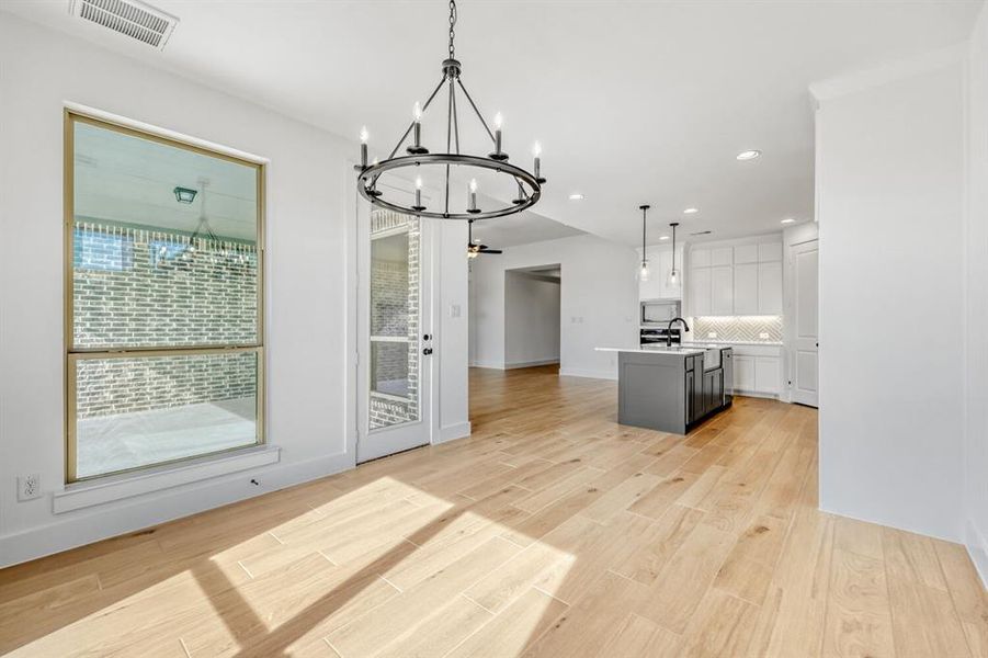 Kitchen featuring open floor plan, an island with sink, light wood finished floors, a chandelier, and decorative backsplash