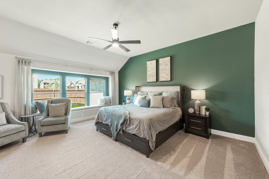 Bedroom with green accent wall, vaulted ceiling, ceiling fan, and large window seat area
