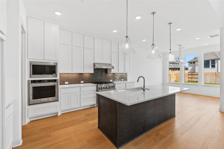 Dual tone kitchen with stainless steel appliances, dual tone cabinetry, tasteful backsplash, an island with sink, and light wood-type flooring