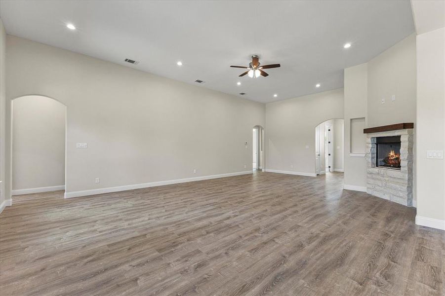 Unfurnished living room with arched walkways, a ceiling fan, a fireplace, light wood-type flooring, and recessed lighting