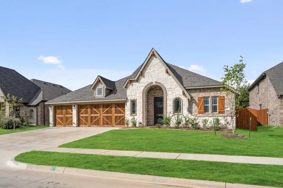 Single-story home with stone and brick exterior, wood garage doors, arched entry, and manicured lawn
