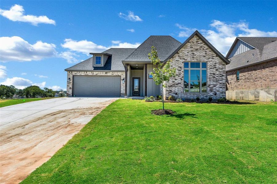 View of front facade featuring concrete driveway, a front yard, a garage, and brick siding