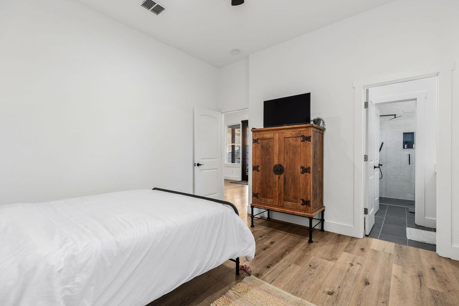 Bedroom featuring light wood finished floors, ensuite bathroom, and a ceiling fan