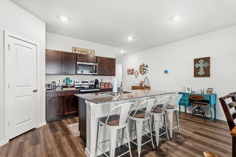 Kitchen featuring a kitchen bar, stainless steel appliances, dark stone countertops, dark wood finish cabinetry, and an island with sink