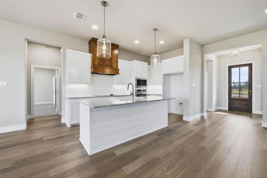 Kitchen with white cabinetry, decorative light fixtures, dark wood-type flooring, light stone counters, and recessed lighting