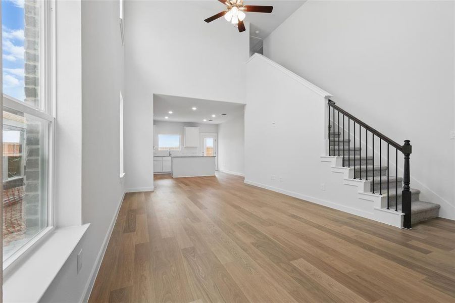 Unfurnished living room featuring a ceiling fan, a towering ceiling, stairway, light wood-style floors, and baseboards Unfurnished living room featuring a ceiling fan, a towering ceiling, stairway, light wood-style floors, and baseboards