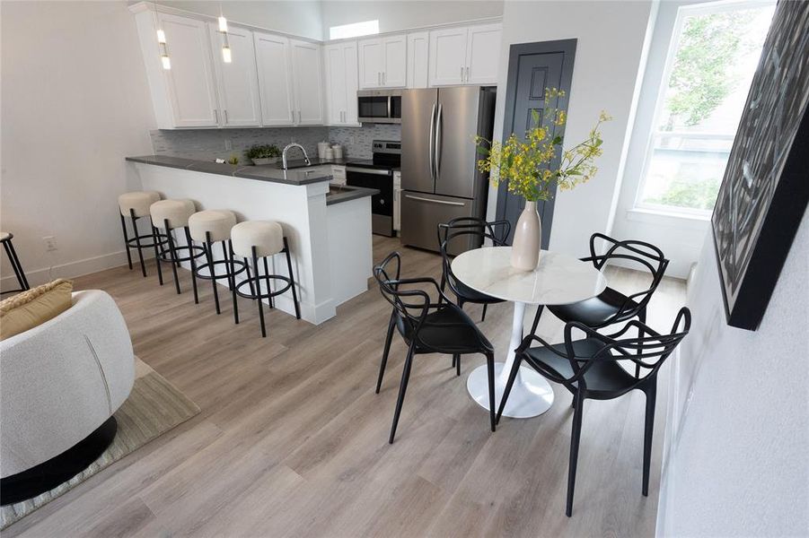 Kitchen featuring white cabinetry, stainless steel appliances, tasteful backsplash, light hardwood / wood-style flooring, and kitchen peninsula