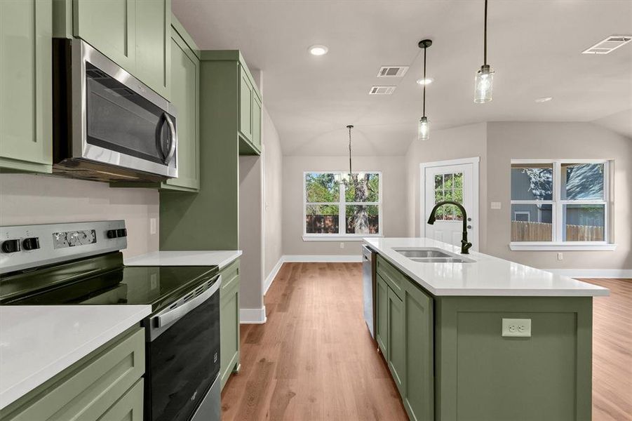 Kitchen featuring green cabinets, stainless steel appliances, light wood finished floors, vaulted ceiling, and light stone counters Kitchen featuring green cabinets, stainless steel appliances, light wood finished floors, vaulted ceiling, and light stone counters