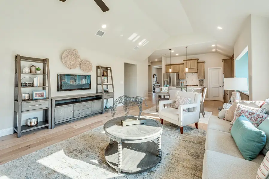 Open-concept living room with vaulted ceiling, hardwood floors, and kitchen visible in background
