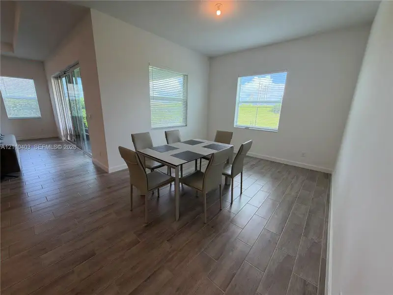 Open-concept area featuring wood-finish tile flooring, neutral wall tones, multi-pane glass sliding doors, and windows with horizontal blinds
