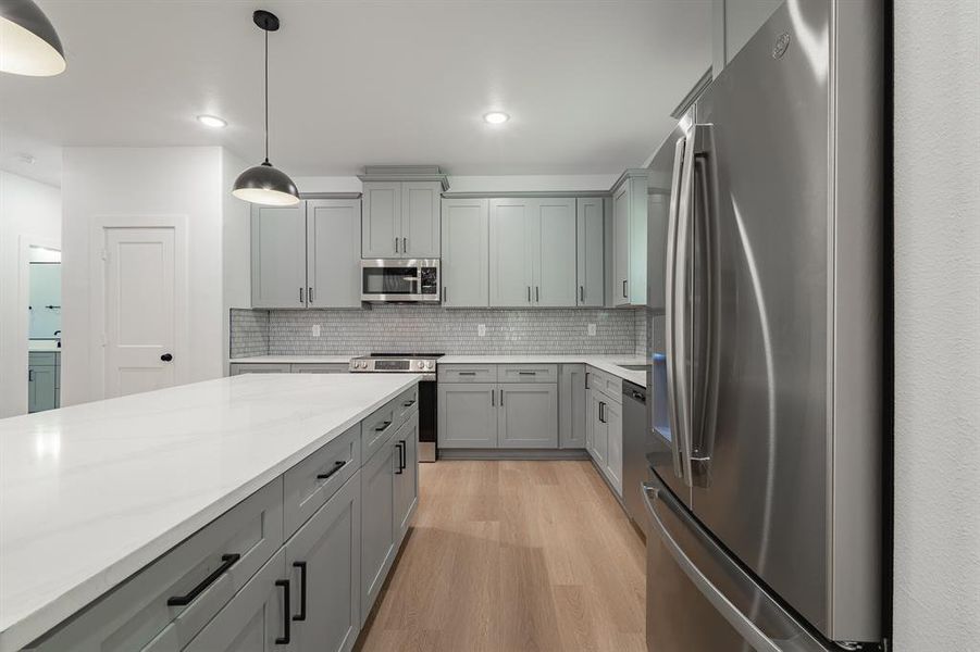 Kitchen with stainless steel appliances, gray cabinets, light wood-type flooring, tasteful backsplash, and pendant lighting Kitchen with stainless steel appliances, gray cabinets, light wood-type flooring, tasteful backsplash, and pendant lighting