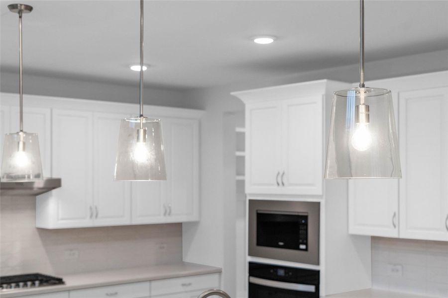 Three exquisite, clear glass pendant lights that elegantly hang above the kitchen island, providing focused task lighting and a touch of refined style. Three exquisite, clear glass pendant lights that elegantly hang above the kitchen island, providing focused task lighting and a touch of refined style.