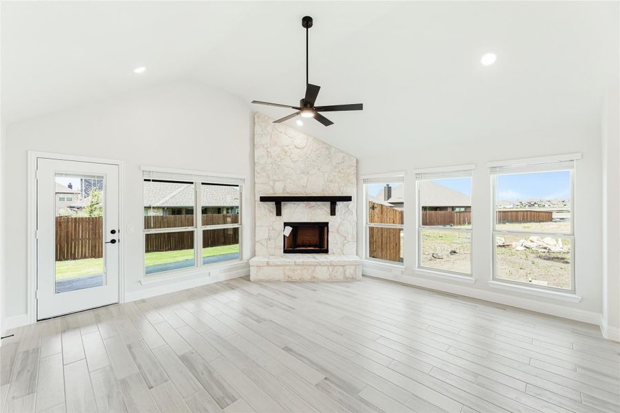 Open living room with stone corner fireplace, vaulted ceiling, ceiling fan, and light hardwood floors