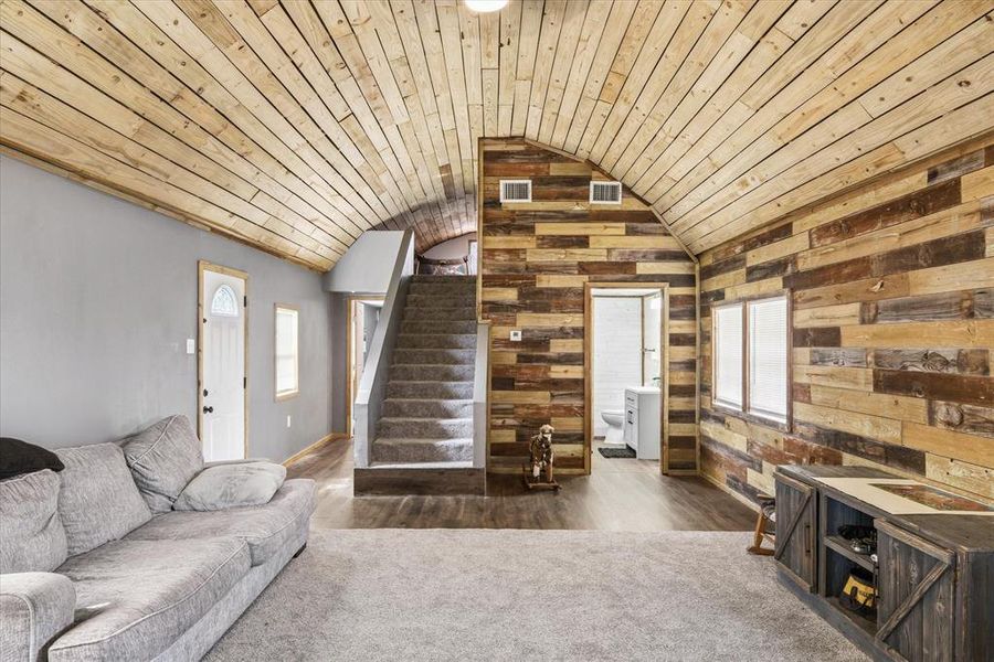 Living room with wooden walls, a vaulted wooden ceiling, plenty of natural light, and dark carpet