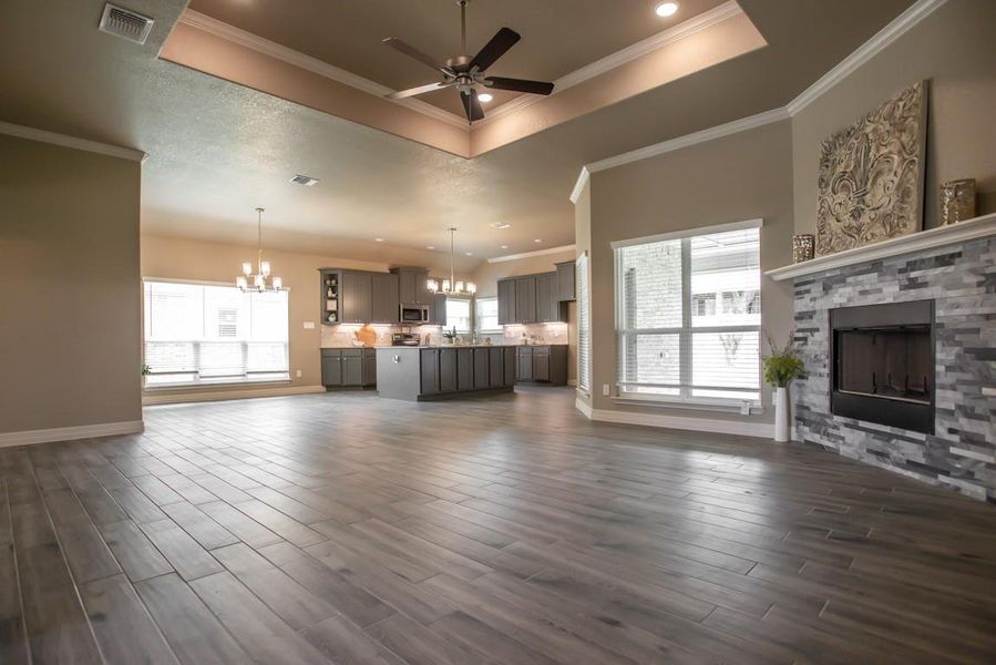 Unfurnished living room with a chandelier, a tray ceiling, a ceiling fan, a stone fireplace, and dark wood finished floors Unfurnished living room with a chandelier, a tray ceiling, a ceiling fan, a stone fireplace, and dark wood finished floors
