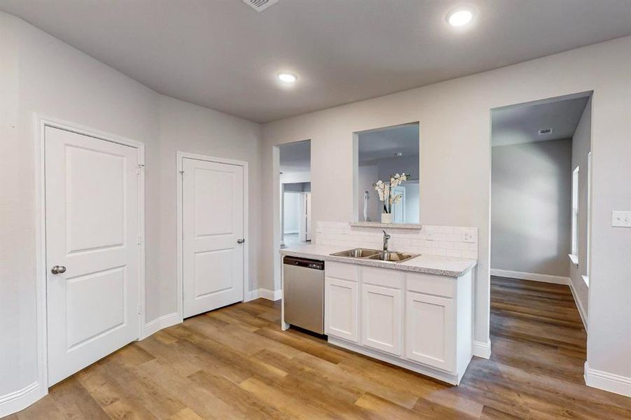 Kitchen with stainless steel dishwasher, sink, white cabinetry, and light wood-type flooring