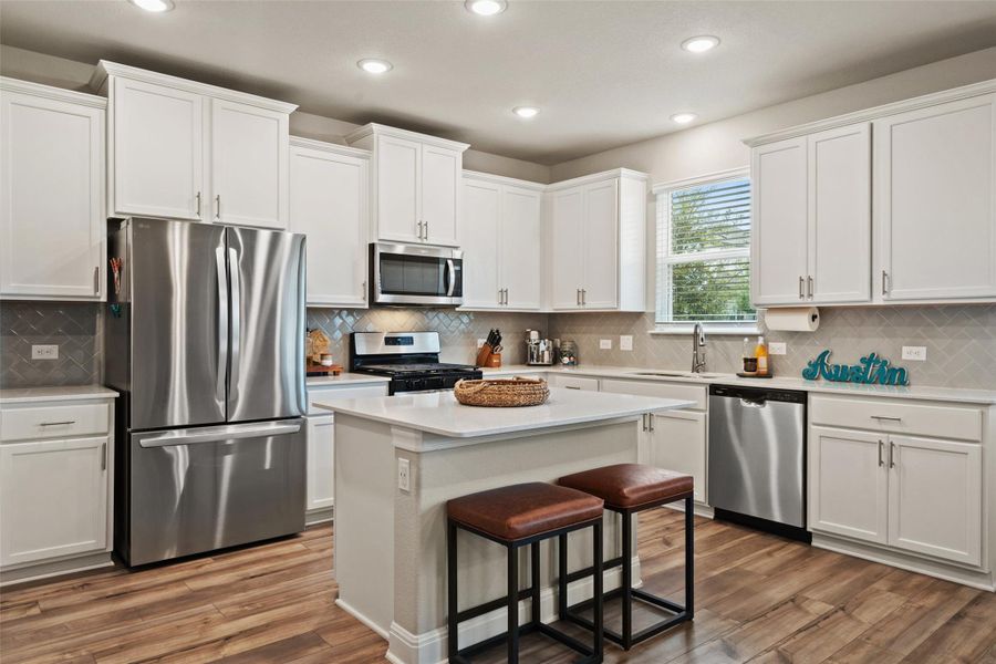 Kitchen with white cabinets, a breakfast bar, wood finished floors, light countertops, and stainless steel appliances