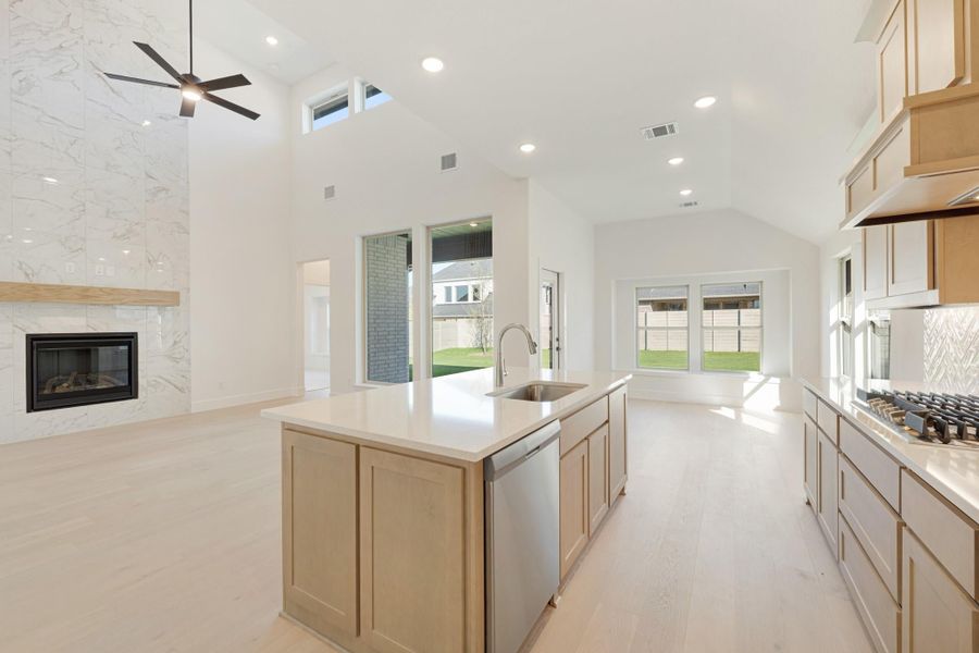 Open-concept kitchen with center island, light wood cabinets, and marble fireplace wall under vaulted ceiling