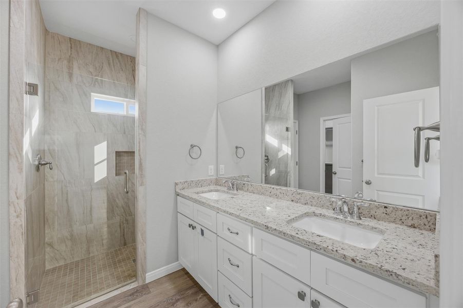 Dual vanity with elegant stone counters and a spacious walk-in shower complete this inviting primary bath.