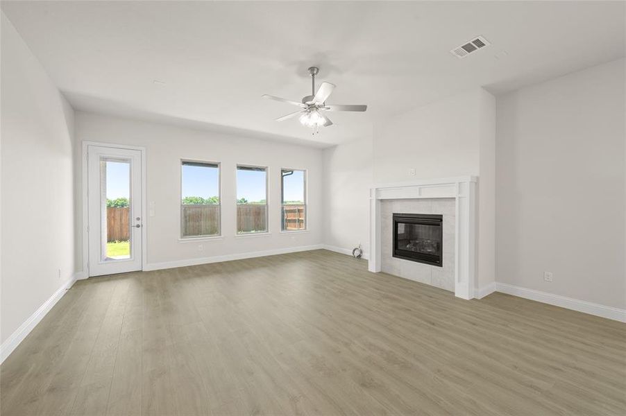 Unfurnished living room featuring wood finished floors, a ceiling fan, and a tiled fireplace
