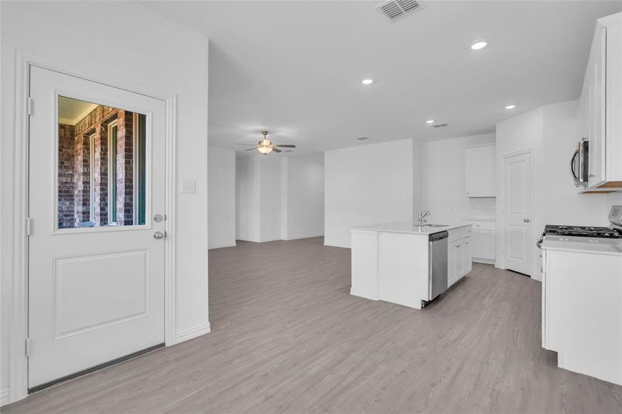 Kitchen featuring white cabinets, light hardwood / wood-style flooring, a center island with sink, appliances with stainless steel finishes, and ceiling fan