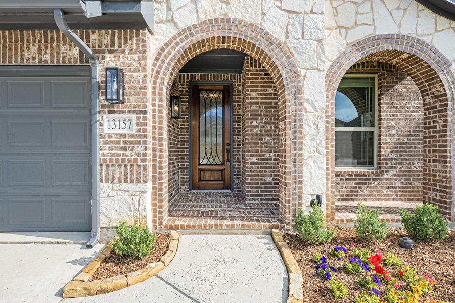 Brick and stone home exterior with arched entryway, wood front door, and attached garage at address 13157