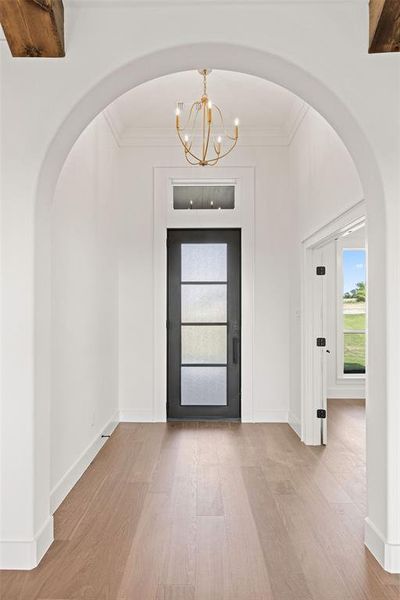 Foyer featuring an inviting chandelier, wood finished floors, arched walkways, crown molding, and baseboards