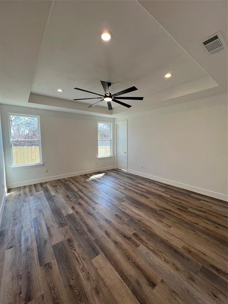 Empty room featuring a ceiling fan, dark wood-type flooring, a tray ceiling, and recessed lighting