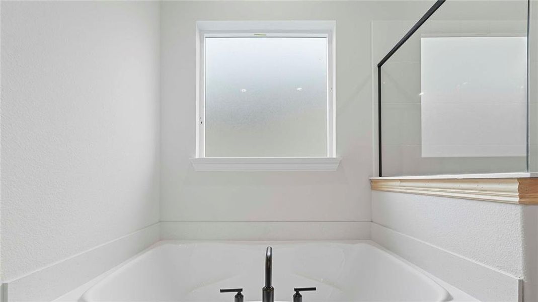 Built-in soaking tub with matte black fixtures, framed by a clear glass shower panel with black trim