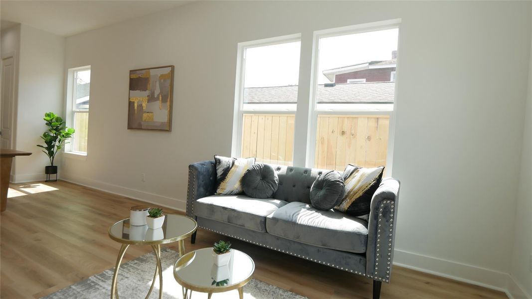 Bright and airy living space with large windows, light wood flooring, and modern decor. Features a stylish gray sofa, accent tables, and artwork, creating a cozy and inviting atmosphere. Bright and airy living space with large windows, light wood flooring, and modern decor. Features a stylish gray sofa, accent tables, and artwork, creating a cozy and inviting atmosphere.