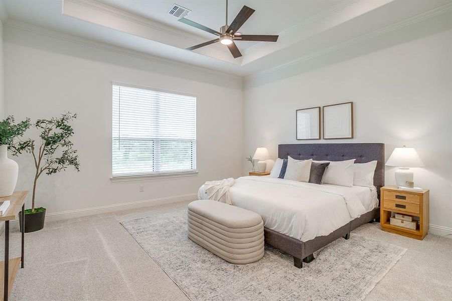 Large primary bedroom with a raised ceiling, crown molding, and a ceiling fan