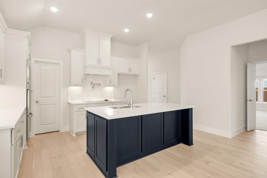 Kitchen with white cabinets, tile backsplash, and navy blue island with white countertop on light hardwood floors
