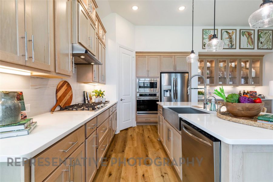 Kitchen featuring tasteful backsplash, glass insert cabinets, stainless steel appliances, light wood-style flooring, and decorative light fixtures Kitchen featuring tasteful backsplash, glass insert cabinets, stainless steel appliances, light wood-style flooring, and decorative light fixtures