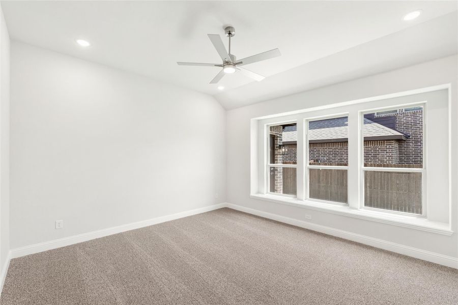 Empty bedroom with carpet flooring, ceiling fan, vaulted ceiling, and large triple window with white trim