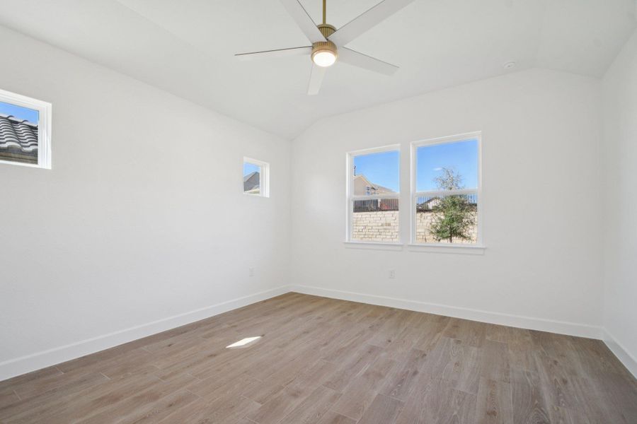 Empty room featuring lofted ceiling, light wood-style flooring, and a ceiling fan