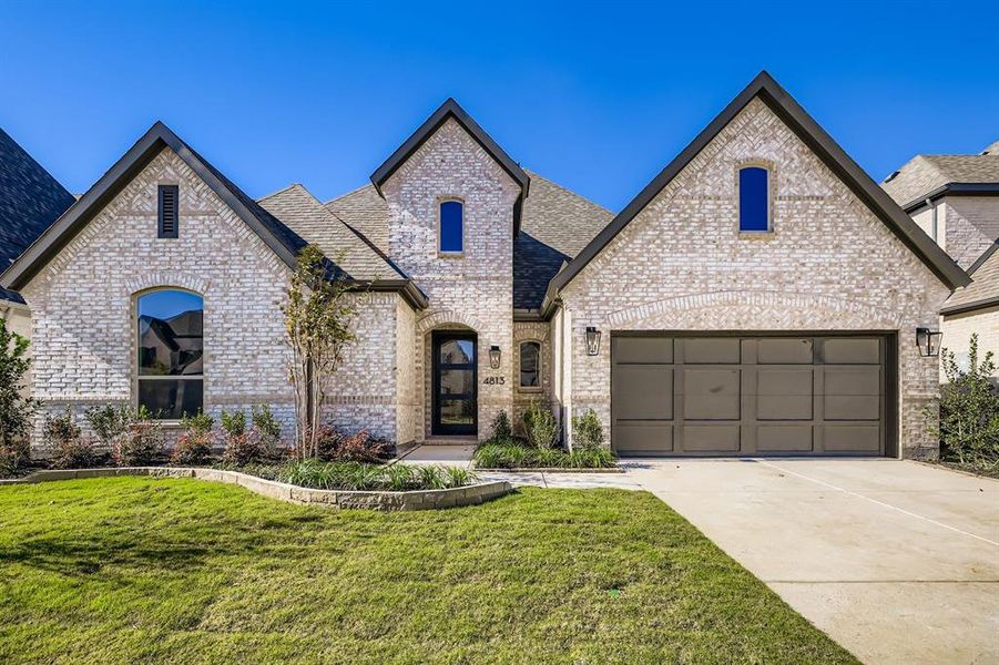 French provincial home featuring brick siding, a front yard, driveway, a garage, and a shingled roof French provincial home featuring brick siding, a front yard, driveway, a garage, and a shingled roof