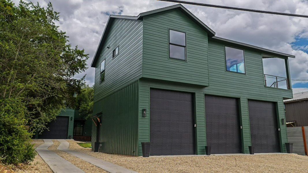 Nature green siding adorns this contemporary secondary residence, featuring an upper-level balcony and multiple possibilities for the oversized garage. Nature green siding adorns this contemporary secondary residence, featuring an upper-level balcony and multiple possibilities for the oversized garage.