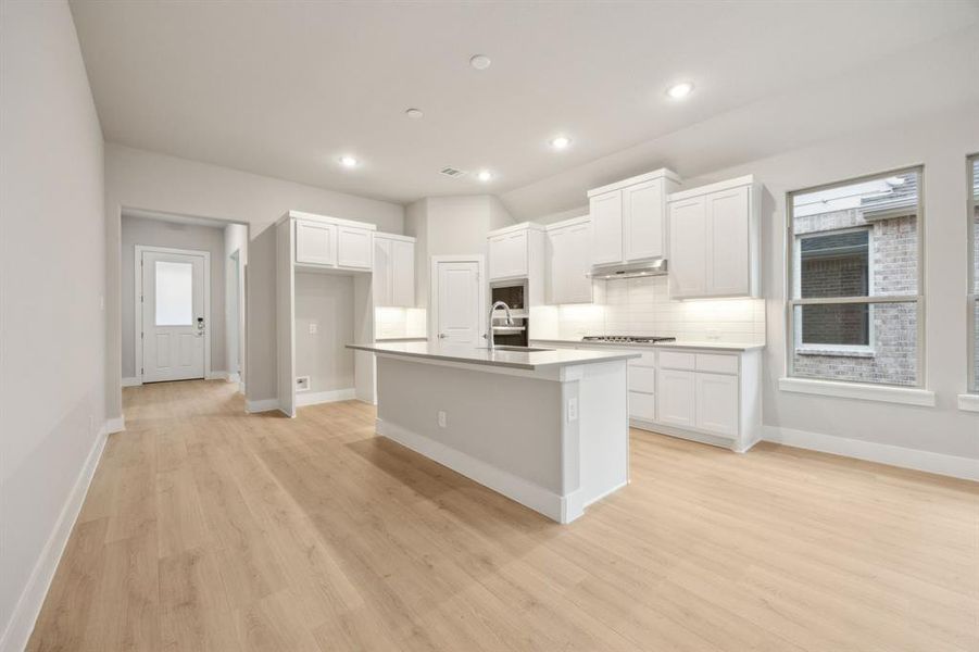 Kitchen with a kitchen island with sink, stainless steel gas cooktop, white cabinets, decorative backsplash, and light wood-type flooring