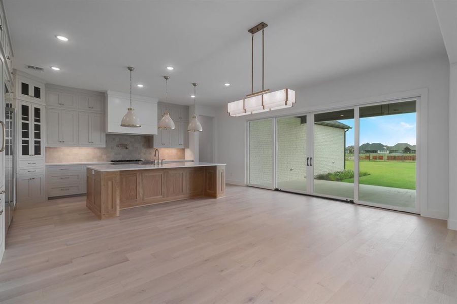 Kitchen with light hardwood / wood-style floors, a large island with sink, and backsplash