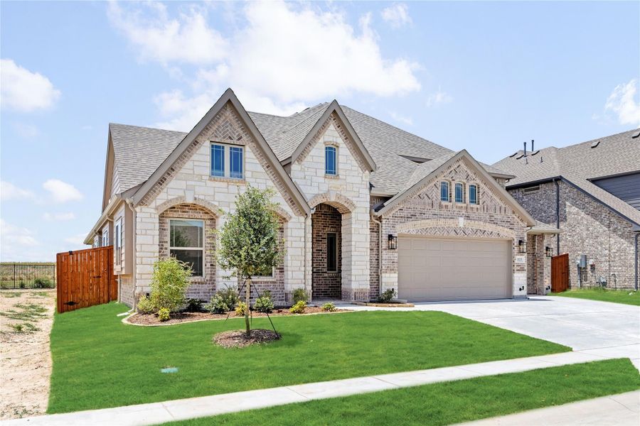 Two-story brick and stone home with arched entry, two-car garage, and landscaped front yard