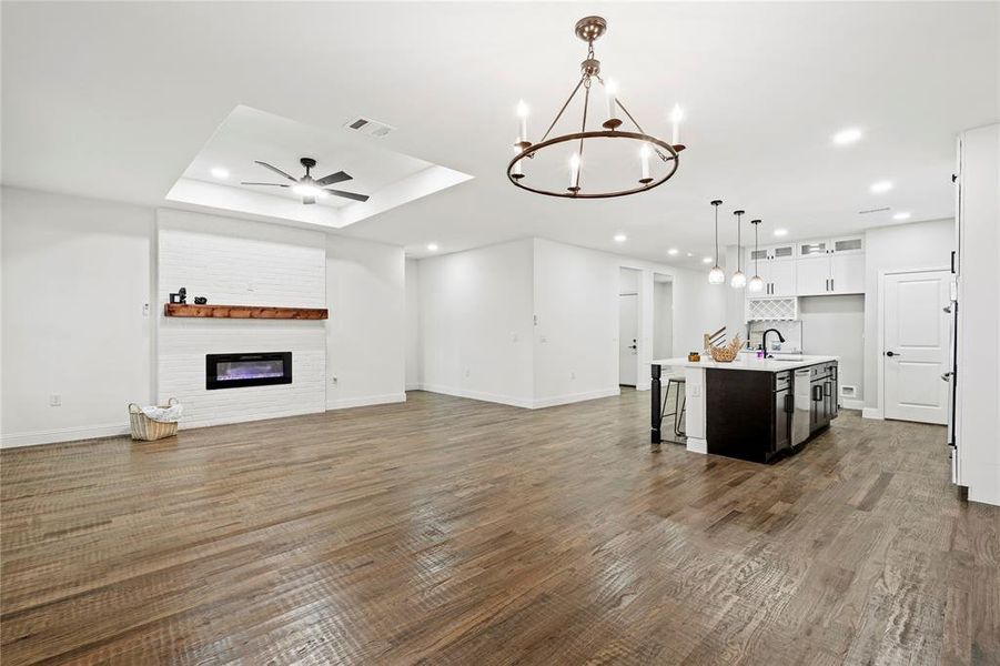 Kitchen featuring open floor plan, an island with sink, white cabinetry, a chandelier, and hanging light fixtures