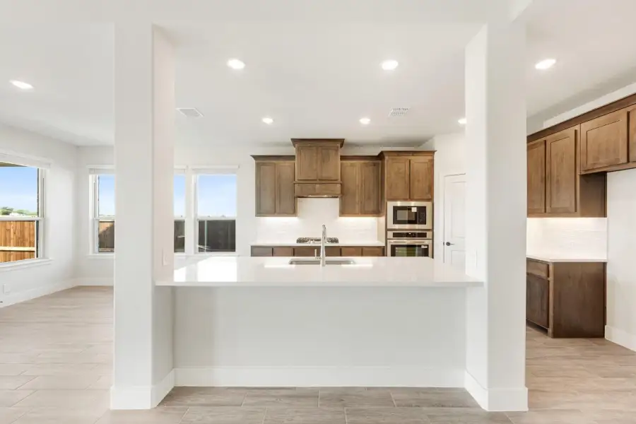 Kitchen with large white island, brown wood cabinets, stainless steel appliances, and tile floors
