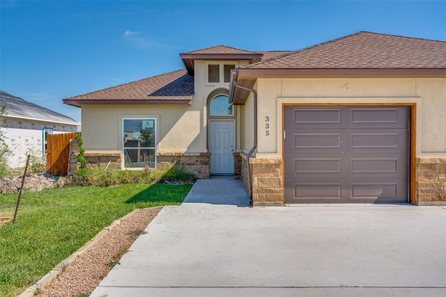 View of front of house featuring a shingled roof, stone siding, stucco siding, and a garage