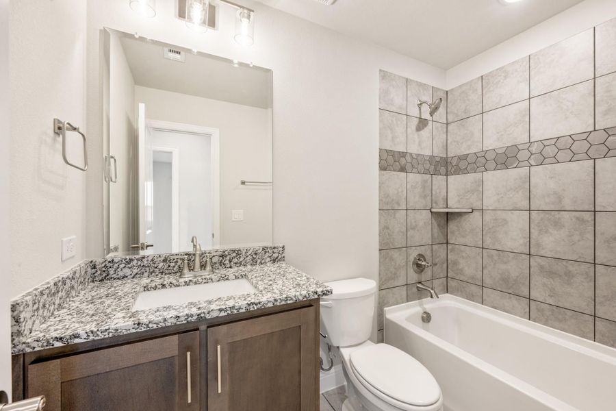 Bathroom with granite vanity, dark wood cabinets, and tiled tub-shower combo with hexagon accent border