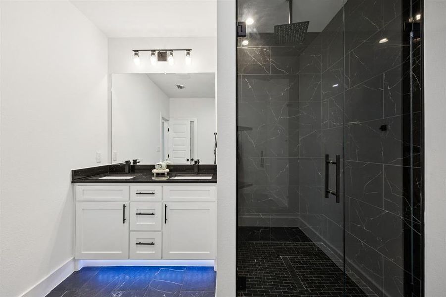 Full bathroom featuring double vanity, dark marble finish floors, and a marble finish shower