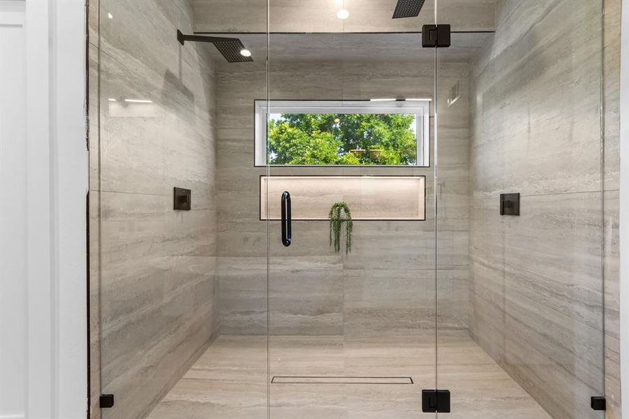 Frameless glass shower enclosure featuring large format stone-look tile, dual rainfall showerheads, an illuminated niche, and a linear drain Frameless glass shower enclosure featuring large format stone-look tile, dual rainfall showerheads, an illuminated niche, and a linear drain