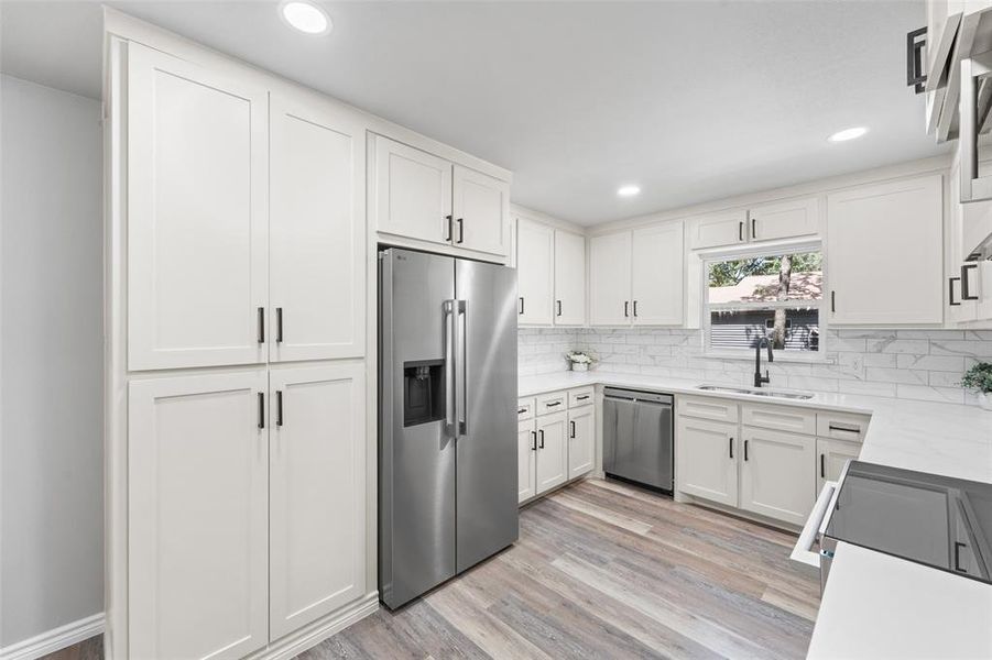 Modern kitchen featuring white shaker cabinetry, stainless steel appliances, wood-finish flooring, white countertops, and a subway tile backsplash Modern kitchen featuring white shaker cabinetry, stainless steel appliances, wood-finish flooring, white countertops, and a subway tile backsplash