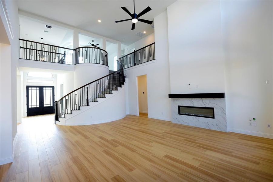 Unfurnished living room featuring a high ceiling, light wood-style floors, a premium fireplace, stairway, and french doors Unfurnished living room featuring a high ceiling, light wood-style floors, a premium fireplace, stairway, and french doors